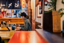 Молодая азиатка в свитере ест за деревянным столиком в кафе — стоковое фото
