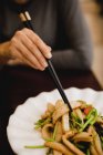 Weibchen essen gekochten Tintenfisch mit Gemüse und Essstäbchen in asiatischem Café — Stockfoto