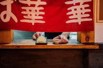Erntehelfer stellt asiatisches Gericht mit Sauce auf Holzbrett mit rotem Tuch auf Fenster im Café — Stockfoto