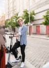 Hombre étnico enfocado utilizando la aplicación para compartir en el teléfono inteligente y el alquiler de bicicletas estacionadas en la calle de la ciudad - foto de stock