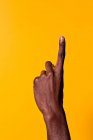 Crop forearm and hand of african-american man raising his index finger against yellow background — Stock Photo