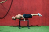 Vue latérale du sportif barbu faisant de l'exercice sur des barres contre un mur rouge pendant l'entraînement dans la salle de gym — Photo de stock