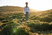 Full body of happy ethnic woman with Border Collie dog walking together on trail among grassy hills in sunny spring evening — Stock Photo