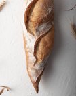 Top view composition of delicious freshly baked rustic artisan baguette placed on white surface with dried wheat spikes — Stock Photo