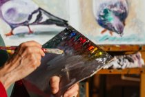 Зверху врожаю невизнана старша жінка-художник змішуючи кольори на палітрі фарби в художній майстерні — стокове фото