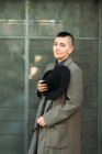 Junger Transgender in edlem Mantel und Hut mit Mohawk blickt bei Tageslicht in die Kamera — Stockfoto
