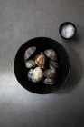 Draufsicht auf Schüssel mit ungekochten Venusmuscheln und Salz, die während der Zubereitung auf einer grauen Tischplatte platziert werden — Stockfoto