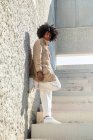 From below side view African American male in vintage coat with Afro hairstyle standing on stairs while looking at camera — Stock Photo