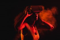 Anonimo stupito femmina etnica con la bocca aperta esplorare realtà virtuale in cuffia su sfondo nero — Foto stock