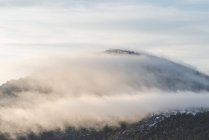 Cerro de montaña cubierto de nieve y bosque verde situado frente al cielo nublado por la mañana en el Parque Nacional Sierra de Guadarrama en Madrid, España - foto de stock