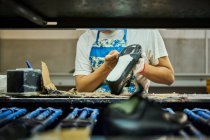 Detalle del trabajador que aplica pegamento a la suela de los zapatos en una línea de producción de fábrica de zapatos chinos - foto de stock