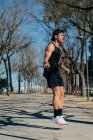 Atleta masculino en ropa deportiva saltando con cuerda y mirando hacia otro lado en la pasarela durante el entrenamiento cardiovascular en el parque - foto de stock