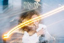 Méconnaissable gai noir guy dans élégant tenue donnant tour de piggyback à petite amie heureuse prenant selfie sur téléphone mobile près de gel des lumières sur la rue — Photo de stock