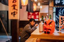 Giovane donna asiatica in maglione mangiare ramen con cucchiaio al bancone di legno in caffè — Foto stock