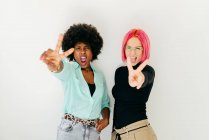 Modern trendy multiracial female friends in stylish outfit shouting while looking at camera and showing v sign on white background — Stock Photo