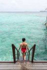Back view of anonymous female in swimsuit going down on stairs into water relaxing in Maldives — Stock Photo
