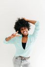 Грайлива молода афроамериканська жінка в модному одязі, яка розважається і показує язик і знак миру на білому тлі. — стокове фото