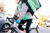 Colheita de baixo ângulo de mensageiro feminino com saco térmico andar de bicicleta na rua ao fazer a entrega no dia ensolarado na cidade — Fotografia de Stock
