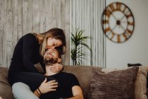 Sorrindo feminino abraçando e beijando o homem alegre na testa enquanto sentado no sofá confortável em casa juntos — Fotografia de Stock