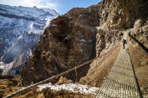 Side view of unrecognizable backpacker standing on metal suspension bridge and admiring view of rocky Himalayas mountains on sunny day in Nepal — Stock Photo