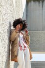 Снизу афроамериканец в винтажном пальто и солнцезащитных очках с прической Афро, стоящей на лестнице, отводя взгляд — стоковое фото