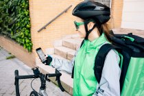 Back view of courier examining route on GPS map before riding bicycle on city street — Stock Photo