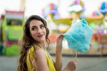 Вид збоку на щасливу жінку, що їсть солодку блакитну бавовняну цукерку, розважаючись та насолоджуючись вихідними на ярмарку влітку — стокове фото