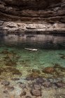 Расслабленная анонимная женщина, плавающая на прозрачной воде провала Бимма в окружении грубых камней во время путешествия по Оману — стоковое фото