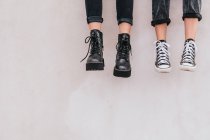 Неузнаваемые женщины в стильных джинсах и обуви сидят на серой стене на городской улице — стоковое фото