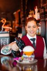 Опытная молодая барменша, используя пылкий дымовой пистолет во время гарнира коктейля у барной стойки — стоковое фото