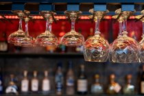 Divers verres en cristal propres de forme et de taille différentes suspendus sur des étagères sur comptoir dans le bar — Photo de stock