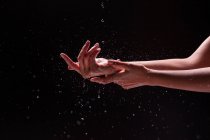 Crop view of anonymous woman washing hands with splashing water against black background — Stock Photo