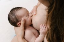 Обрезанная неузнаваемая любящая мать кормящая грудью новорожденного, сидя в комнате дома — стоковое фото