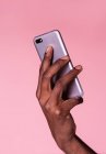 Mãos de colheita de homem afro-americano segurando telefone e fazendo gesto isolado no fundo rosa — Fotografia de Stock