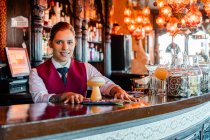 Barman souriante debout au comptoir du bar avec un type de boisson alcoolisée servie dans des verres à cocktail créatifs en forme de champignon — Photo de stock