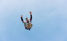 Dal basso del maschio che salta fuori terra ed esegue acrobazie parkour sullo sfondo del cielo blu senza nuvole — Foto stock