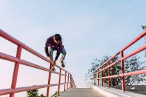 Faible angle courageux jeune homme sautant au-dessus de la rampe en métal en ville tout en effectuant cascade de parkour sur une journée ensoleillée — Photo de stock