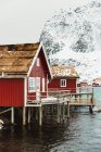 Caminho de madeira que vai perto da parede da cabana na aldeia costeira perto do cume de montanha nevado no dia de inverno em Ilhas Lofoten, Noruega — Fotografia de Stock