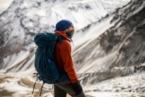 Vista lateral del caminante masculino en ropa interior caliente de pie en la colina sobre el fondo de las montañas nevadas del Himalaya en invierno en Nepal - foto de stock