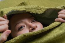 Молода зеленоока жінка дивиться геть, ховаючись за рваною зеленою тканиною — стокове фото