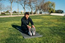 Дорослий спортсмен в спортивному одязі і кросівки, вправи на газоні в місті в сонячний день — стокове фото