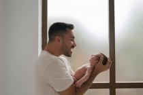 Suave padre de pie con lindo bebé durmiendo cerca de la pared en las ventanas en casa - foto de stock