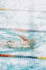 De cima visão traseira de desportista paralímpico irreconhecível em óculos e boné sem mão nadando estilo crawl na piscina entre as pistas — Fotografia de Stock