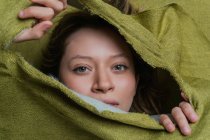 Giovane donna dagli occhi verdi guardando la fotocamera mentre si nasconde dietro un panno verde strappato — Foto stock
