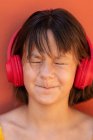 Zufriedenes Kind hört Song von drahtlosem Headset auf orangefarbenem Hintergrund — Stockfoto