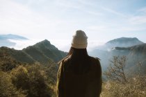 Rückansicht einer nicht wiedererkennbaren Frau in warmer Kleidung, die allein auf einem Aussichtspunkt steht und auf neblige Bergrücken blickt, die flauschige Wolken im Sequoia Nationalpark unter blauem Himmel in den USA bedecken — Stockfoto