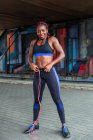 Мускулистая афроамериканская спортсменка, стоящая с скакалкой и улыбающаяся на улице — стоковое фото