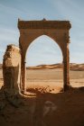 Arco do antigo edifício arruinado localizado no deserto arenoso contra o céu nublado no dia ensolarado perto de Marraquexe, Marrocos — Fotografia de Stock