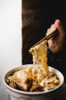 Mão com pauzinhos puxando macarrão enquanto come sopa de macarrão de carne de grande tigela de cerâmica — Fotografia de Stock