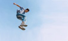 Снизу мужчины прыгают над землей и выполняют паркур трюк на фоне голубого безоблачного неба — стоковое фото